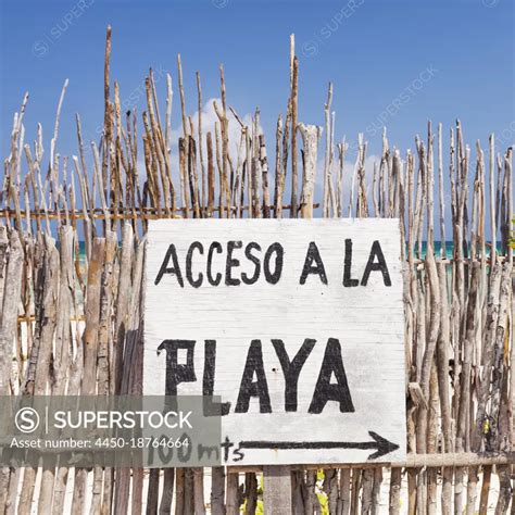 Beach access sign in Spanish, on a fence by the beach - SuperStock