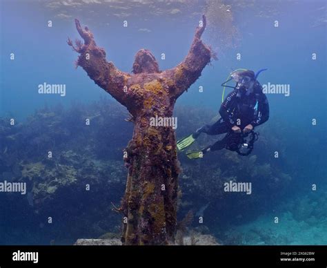Diver with camera looking at an underwater statue of Jesus Christ (Christ of the Abyss), dive ...