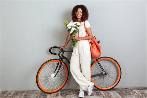 Smiling african woman posing with bicycle, backpack and flowers ...