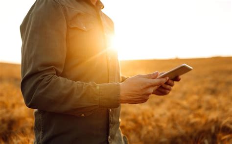 Agricultor em uma máscara estéril com um tablet nas mãos em um campo de ...