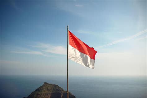 Indonesia national flag waving in the blue sky on the ocean background. Red and white flag with ...