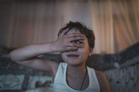 Small emotional boy covers his face with his hand, watching a horror ...