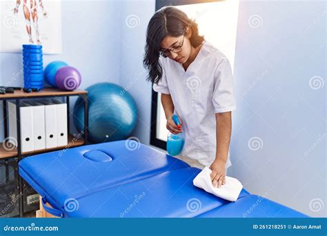 Young Latin Woman Wearing Physiotherapist Uniform Cleaning Massage Table at Physiotherapy Clinic ...