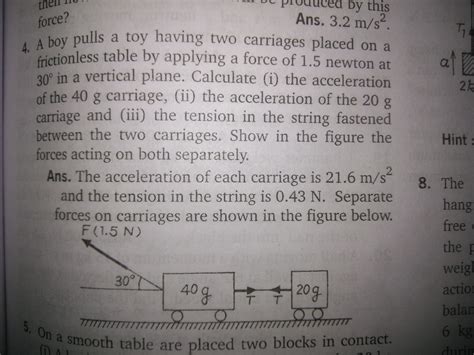 A boy pulls a toy having two carriages placed on a frictionless table ...