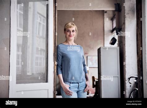 Shamima Begum leaning against a door frame. She has long dyed brown hair and is wearing sunglasses with a light grey top underneath a sweatshirt jacket