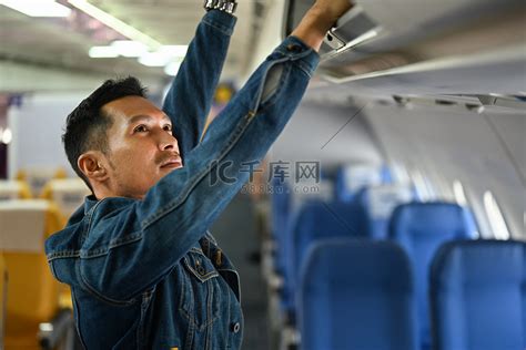 赶时髦的人乘客把他的行李放进飞机的头顶隔间高清摄影大图-千库网