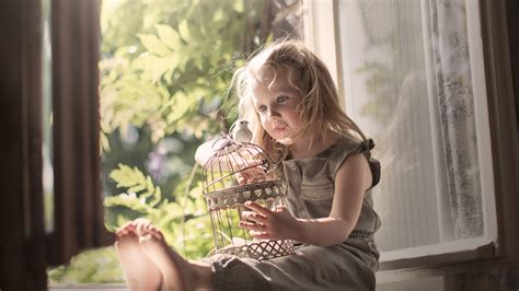 Cute Little Girl Is Sitting Near Window With Bird And Cage On Lap ...