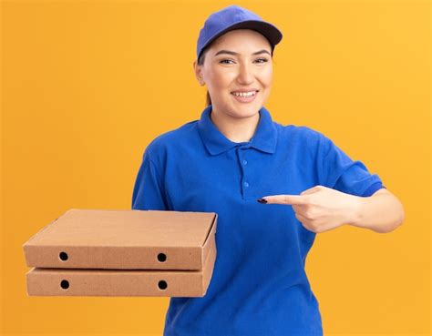 Happy young delivery woman in blue uniform and cap holding pizza boxes ...