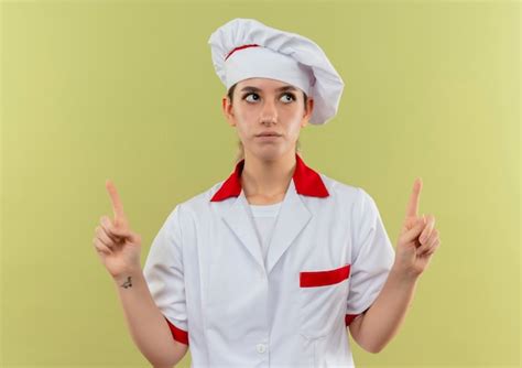 Réfléchi jeune joli cuisinier en uniforme de chef pointant et levant ...