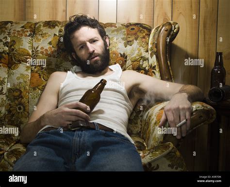 Man on couch with beer bottle and cigarette Stock Photo - Alamy