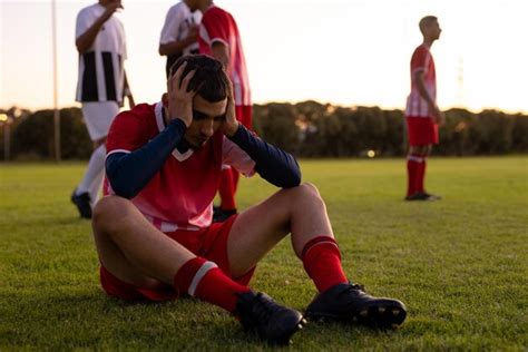 Caucasian sad athlete with head in hands sitting on land with players ...