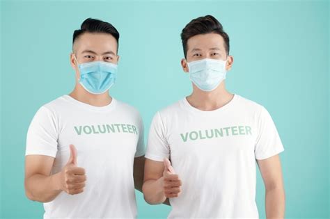 Joyful young men in protective masks working as volunteers during covid ...