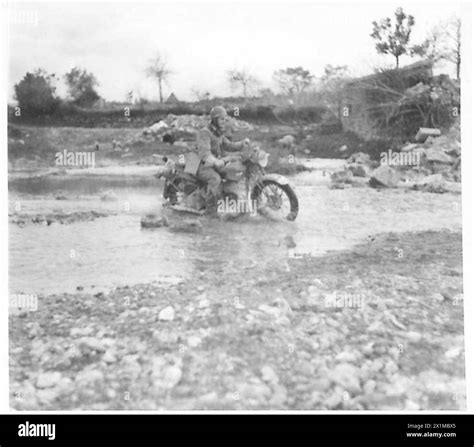 A demolished bridge in Italy forces Eighth Army personnel to ford a river during operations ...