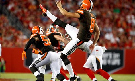 A Cleveland Browns punter executing a kick during a game, with teammates positioned nearby in a crowded stadium.