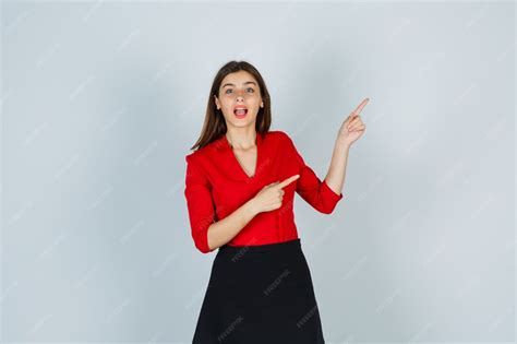 Young woman pointing right with index fingers in red blouse | Free Photo