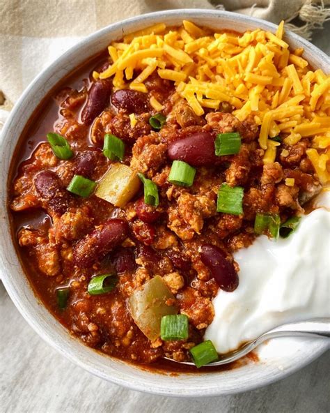 A bowl of Laura's quick slow cooker turkey chili, topped with shredded cheese, sliced green onions,