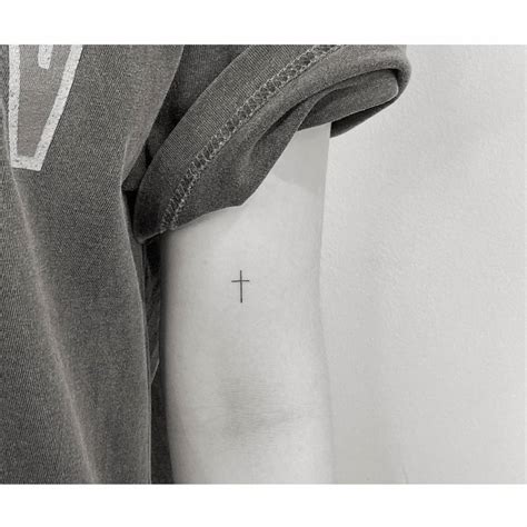 Minimalistic cross tattooed on the bicep.