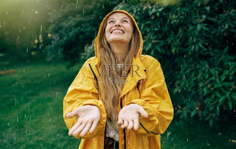 在下雨的公园里，一个穿着黄色雨衣的积极的年轻金发女人的形象。开朗的女性享受户外的雨。女人抬起头，用手接住雨滴。照片摄影图片_ID ...