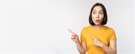 Surprised asian woman pointing and looking left at copy space promo ...