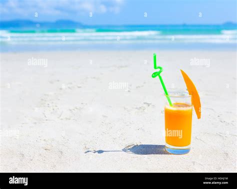 Glass of orange colour juice on the beach. Mango juice and slice on ...