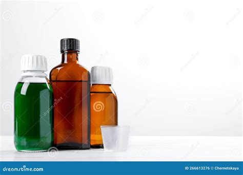 Bottles of Syrups with Measuring Cup on Wooden Table Against White ...
