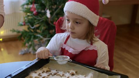 Mother shows to her son how to cover biscuits with sugar powder using ...
