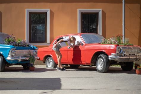 A young woman poses at an abandoned car with a flower garden in place ...