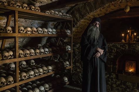 Greek Orthodox monk in front of the skulls of monks that lived in his ...