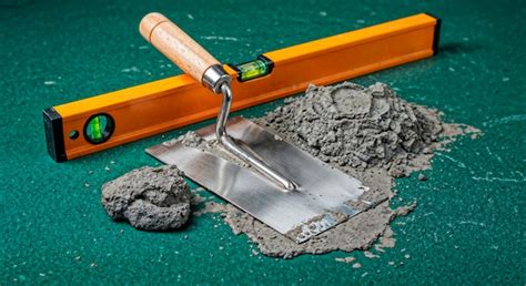 Trowel, cement, and level resting on a green surface, construction ...