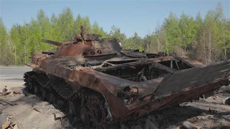 A man walks past a burnt armoured personnel carrier near buildings destroyed in the course of Ukrain