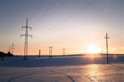 Premium Photo | Electrical tower on a snowy field sun goes down orange ...