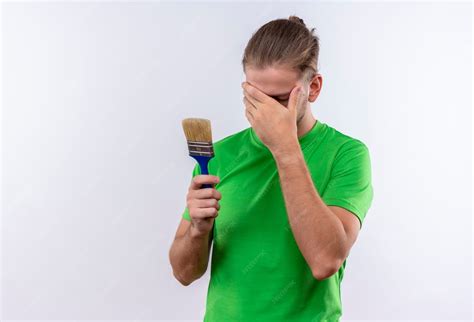 Young handsome man in green t-shirt holding paint brush covering face ...