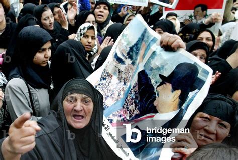 Black-and-white photo of Saddam Hussein, in a suit, with a group of women students