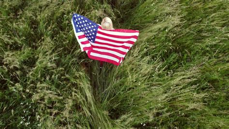full length blond Woman holding American Flag in trees shadow of ...