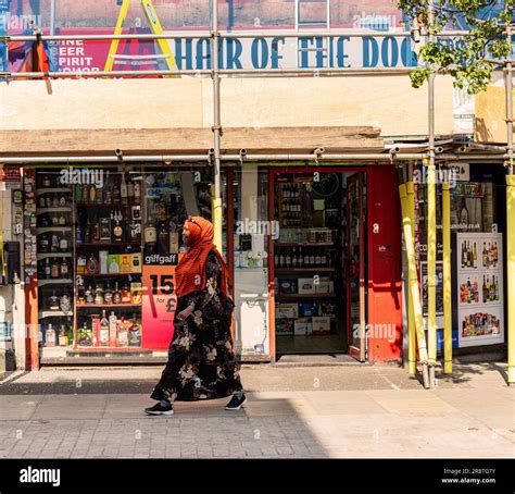 Woman in Muslim dress walking down the North End Road, Fulham, London, past an off-licence ...