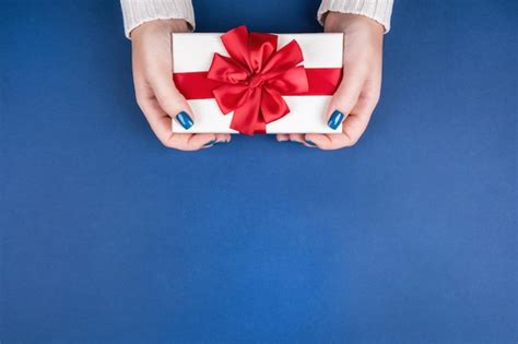 A large gift box with a red bow in well-groomed female hands on a blue ...