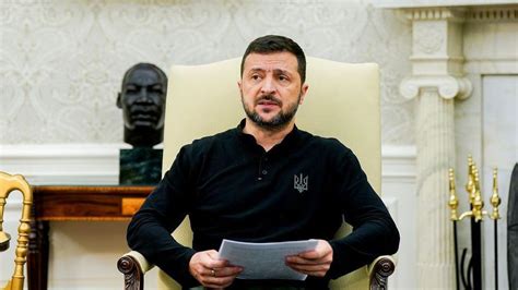 Zelensky wearing a green shirt speaks in a dimly-lit room. An out-of-focus Christmas tree is in the