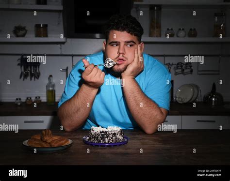Depressed overweight man eating cake in kitchen at night Stock Photo ...