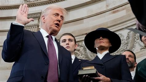 Trump, with his family watching, raises his right hand and places his left hand on the Bible as he t