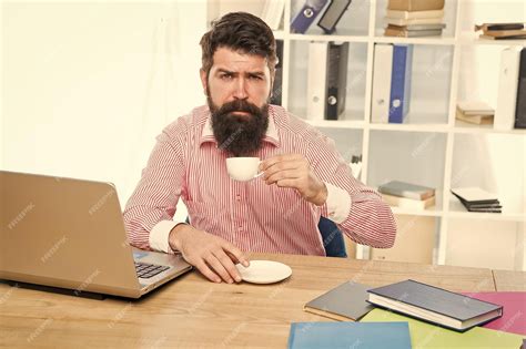 Premium Photo | Exhausted clerical worker with hipster beard drink coffee sitting at desktop in ...