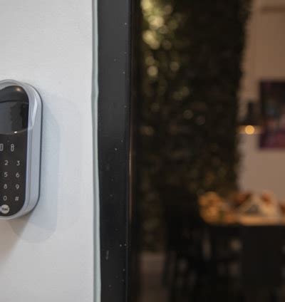 A smart digital lock with a keypad is mounted on a white wall. In the ...