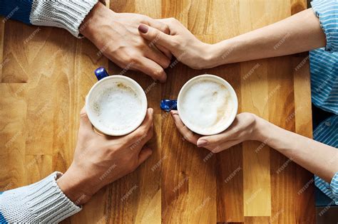 Couple holding hands and coffee cups at cafe table | Premium Photo