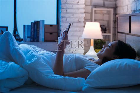 亚洲女性晚上睡觉前会在床上使用智能手机。手机成瘾的概念。照片摄影图片_ID:300001682-Veer图库