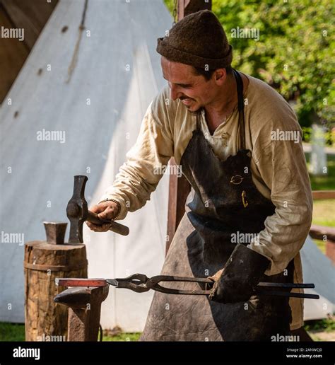 A blacksmith dressed in a medieval costume works in a forge. Forge in ...