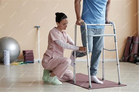 Professional therapist helping patient to walk using walker during ...