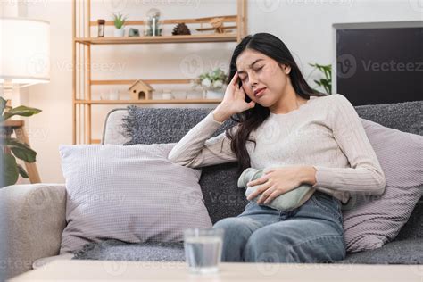 Young Woman Experiencing Abdominal Pain and Headache During Menstruation While Sitting on a Sofa ...
