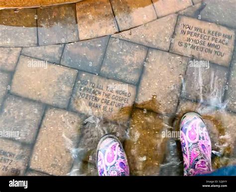 Bright rain boots splash in rainwater puddle beside fountain base and ...