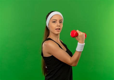 Young fitness woman in sportswear with headband holding dumbbell doing ...