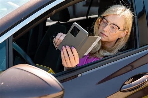 A middle aged blonde woman in glasses with a smartphone looks through ...