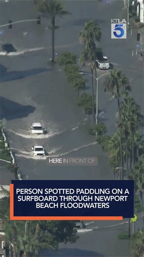 Person spotted paddling on a surfboard through Newport Beach floodwaters